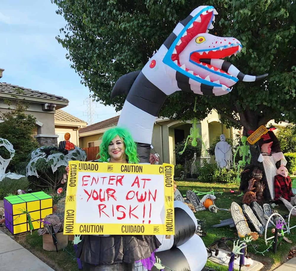 Colorful Halloween yard display with a woman in costume holding a warning sign about entering at your own risk.