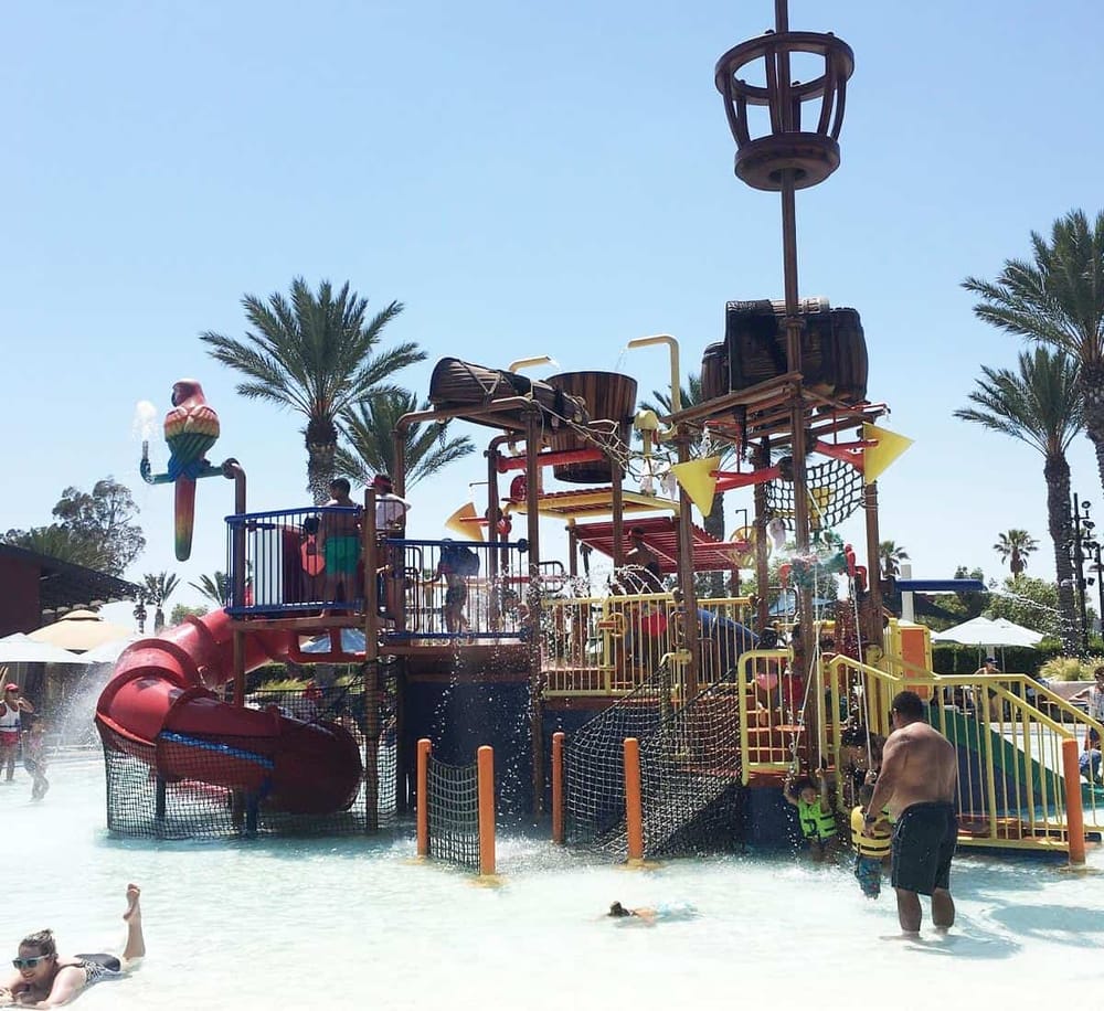 Colorful water park splash structure with children playing and palm trees in the background, perfect for family fun.