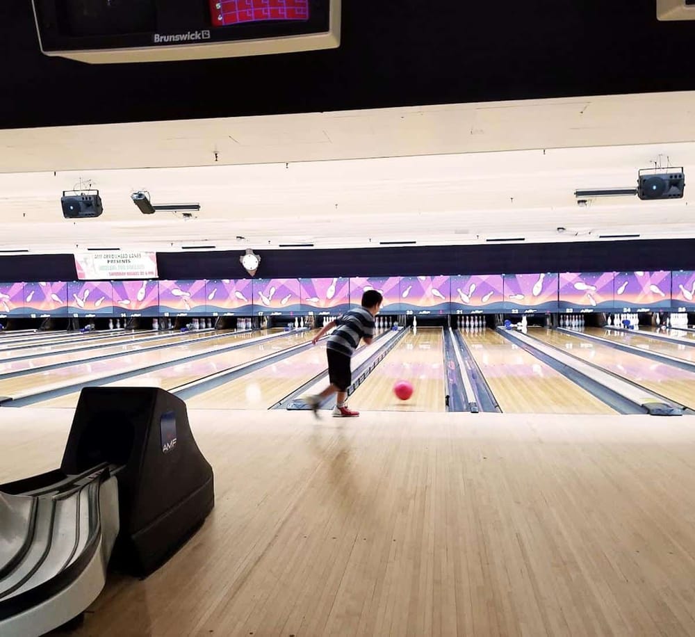 Child bowling at bowling alley with digital scoring screen in background.