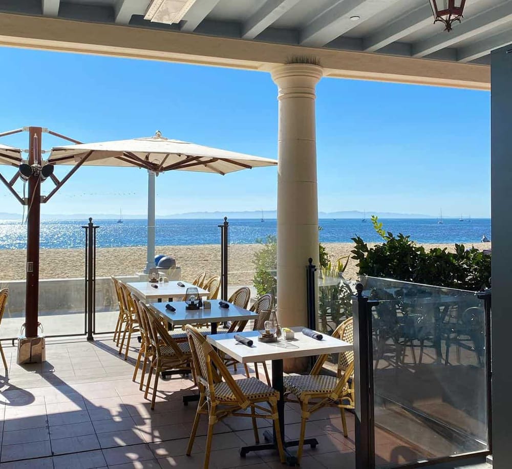 Outdoor beachside dining area with ocean view and umbrellas, perfect for a relaxing seaside meal.