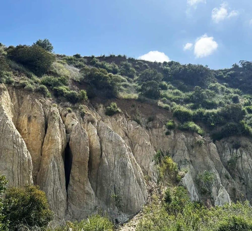 Vast hillside with rocky cliffs, lush green shrubs, and blue sky in the background.