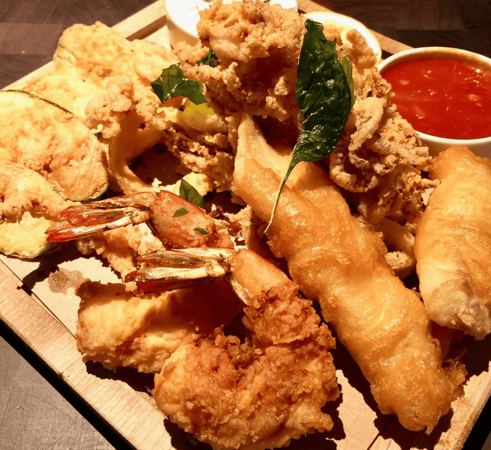 Deep-fried seafood platter with shrimp, fish, and dipping sauces at a casual restaurant.