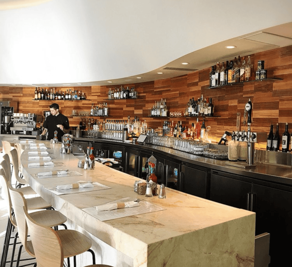 Spacious modern bar with barista and selection of liquor bottles, elegant interior design.