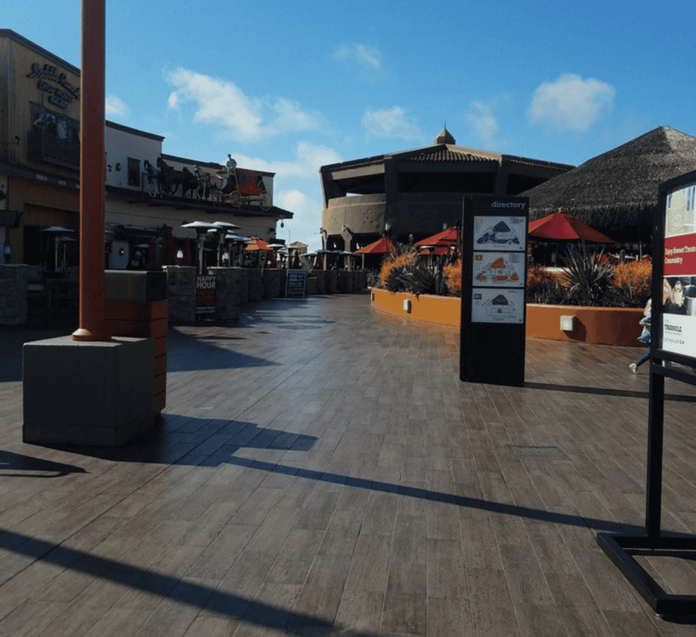 Open-air shopping plaza with directory sign, outdoor seating, and decorative plants.