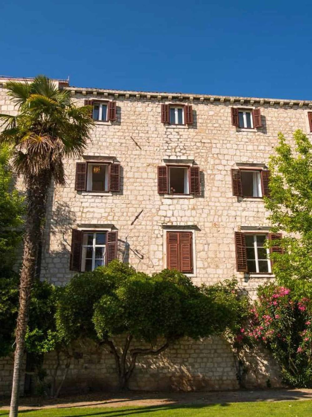 Charming stone building with wooden shutters and lush greenery, perfect for travel and vacation destinations.