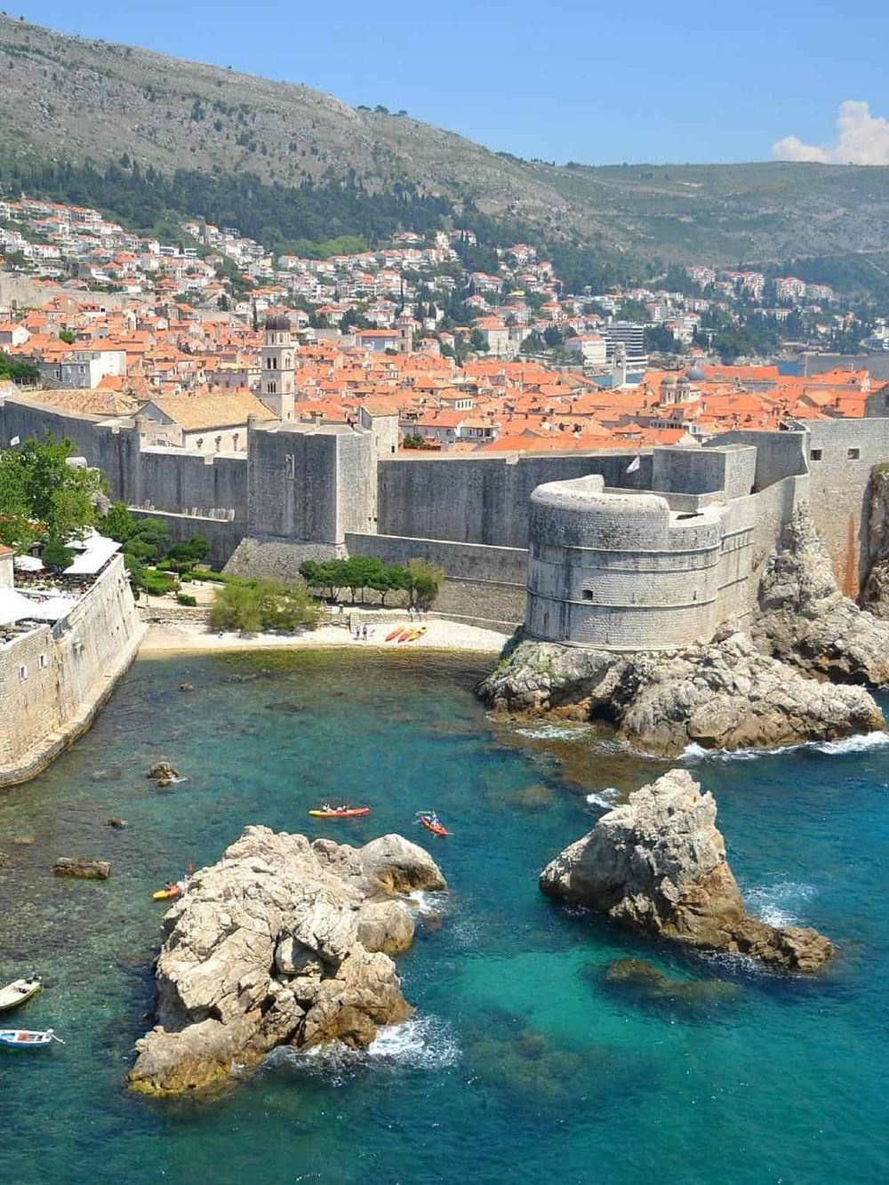 Historic Dubrovnik city walls along the Adriatic Sea, Croatia, with red rooftops and turquoise waters.