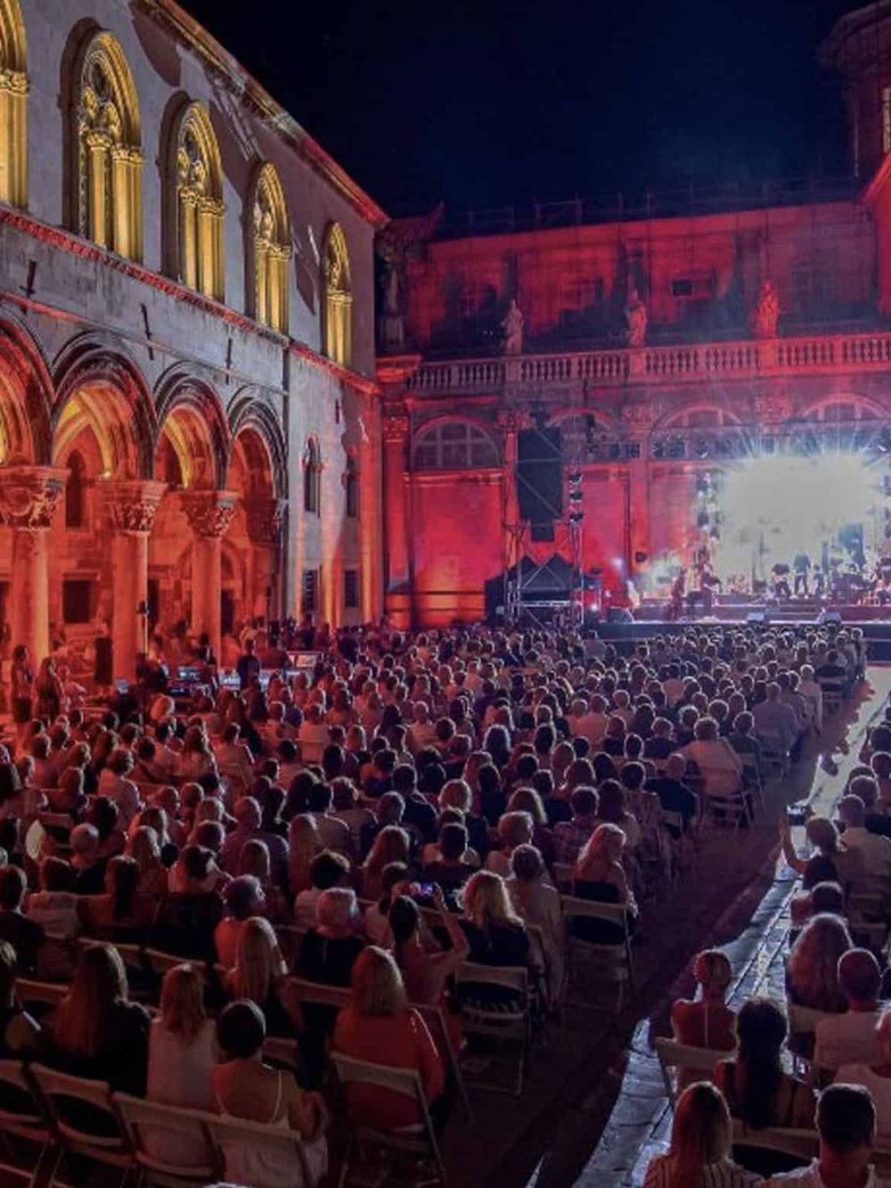 Spectacular outdoor concert at historic venue with illuminated architecture and vibrant stage lighting.