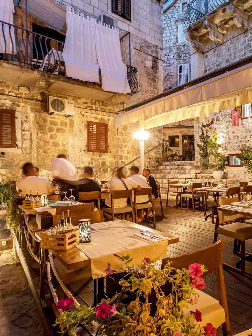 Cozy outdoor restaurant seating area in historic stone building with string lights and lush plants.