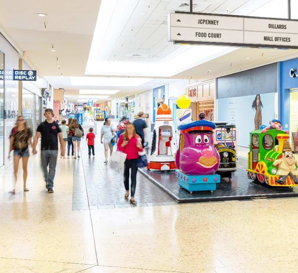 Bright indoor shopping mall with colorful children’s rides near store entrances.