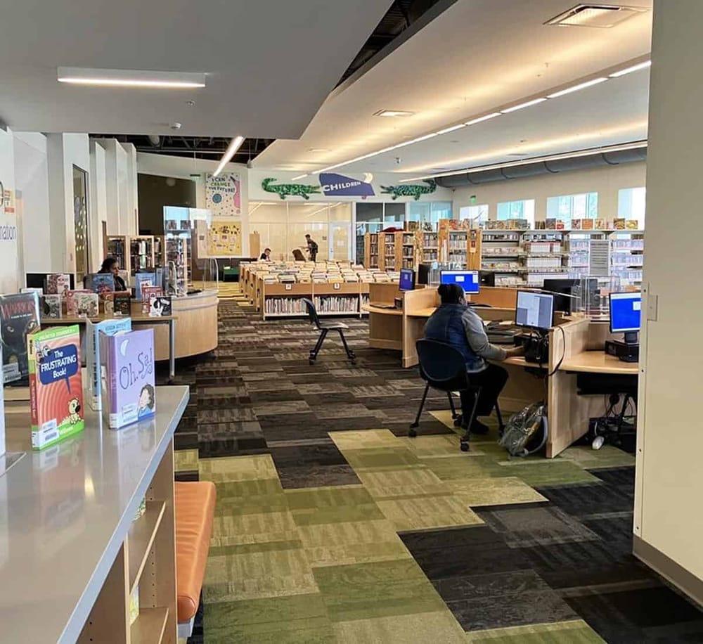 Bright public library interior with computer stations and children’s book section, focused on reading and research resources.