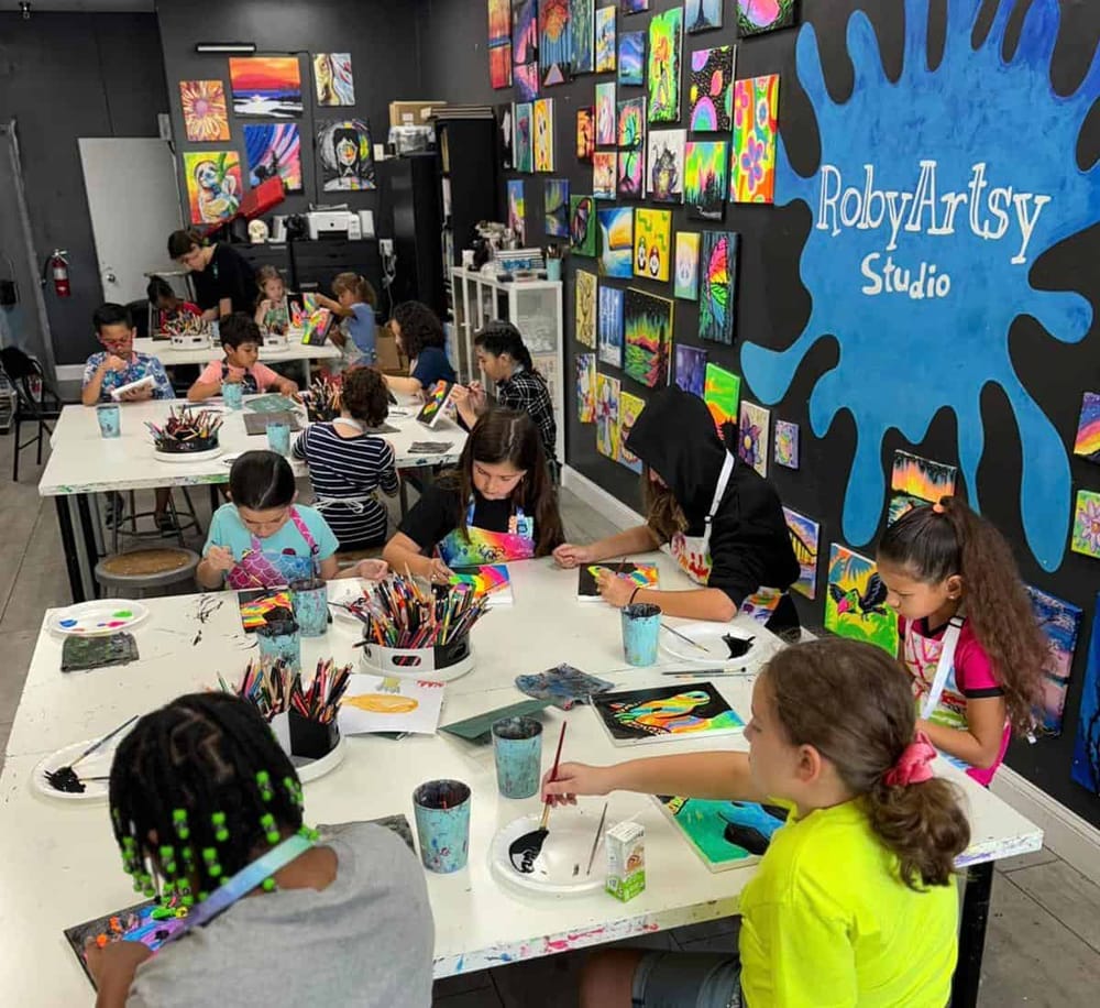 Vibrant kids' art class at RobyArtsy Studio with colorful paintings on wall and children creating masterpieces.