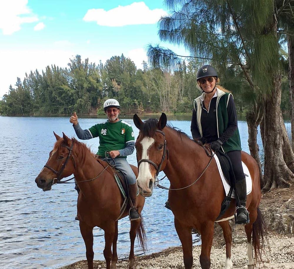 1. People horseback riding near a lakeside with trees and blue sky.