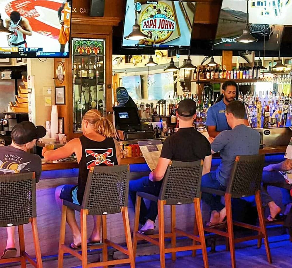 Bright bar scene at a sports restaurant with patrons enjoying drinks and television screens showing sports games.