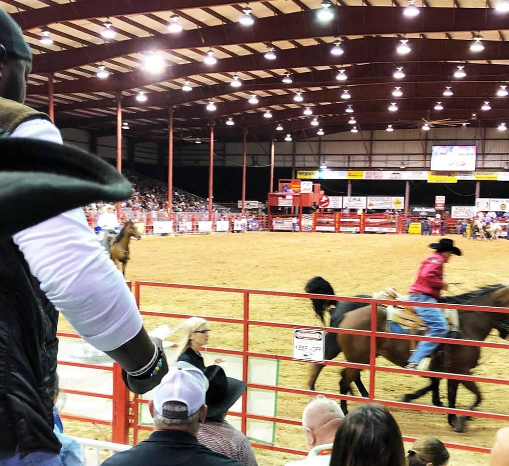 Rodeo arena during a cattle riding event at QuestForDirections rodeo grounds. Spectators watch as cowboys ride horses.
