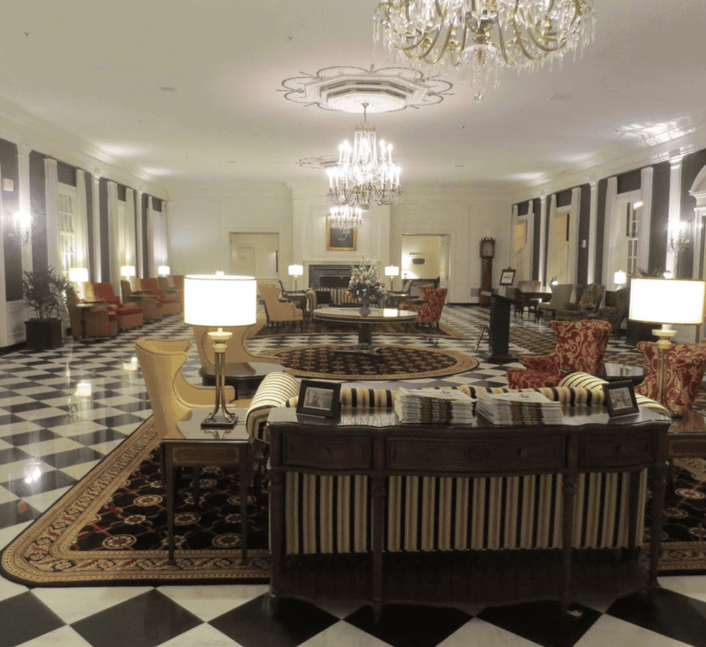 Elegant hotel lobby with chandeliers, luxurious furniture, black and white checkered flooring, and classic decor.