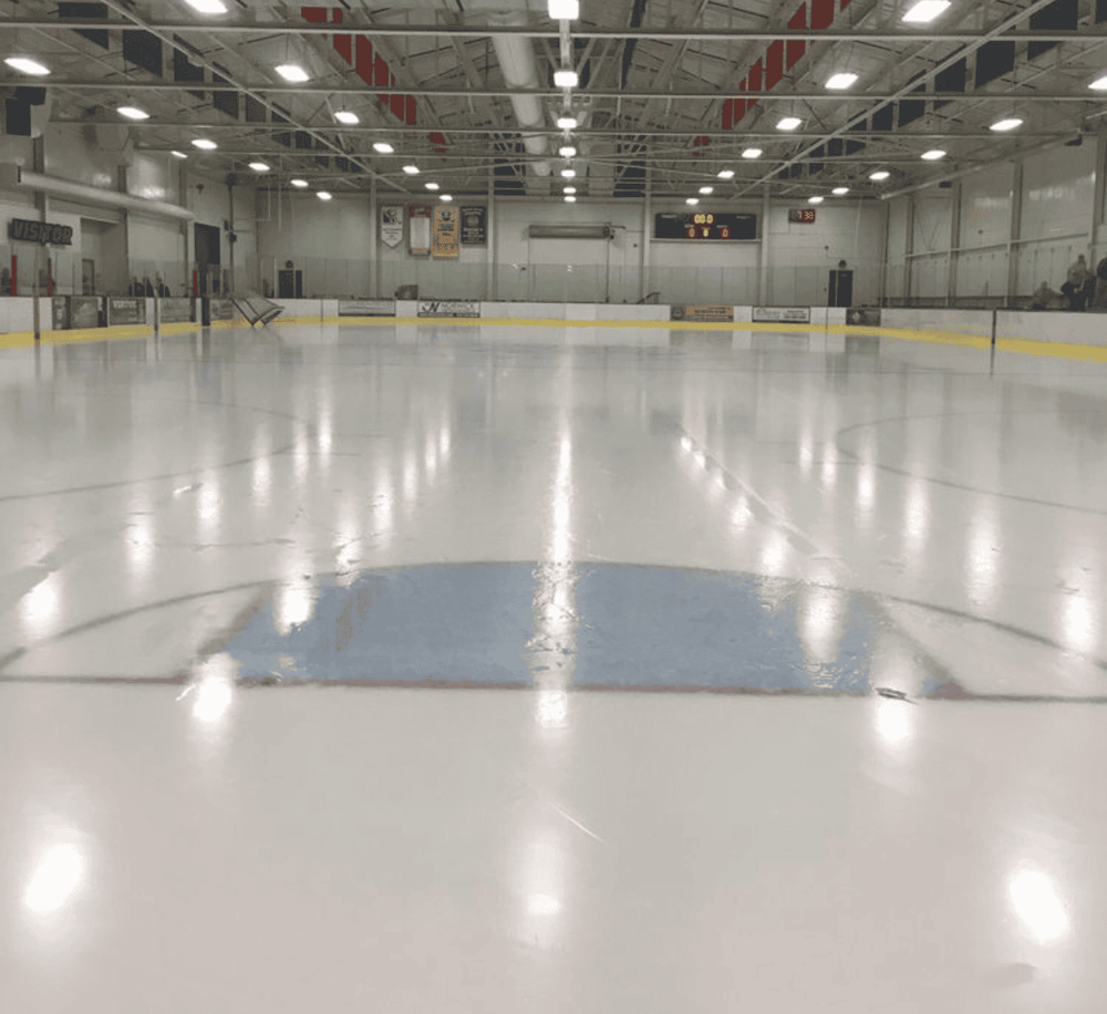 Shiny indoor ice hockey rink with empty playing surface and surrounding seating area.