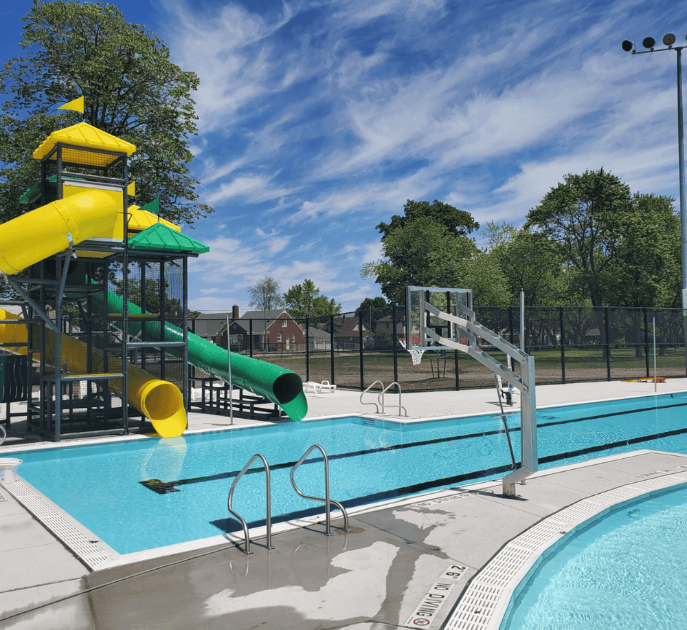 Colorful backyard water slide and pool with sunny sky and trees in the background.