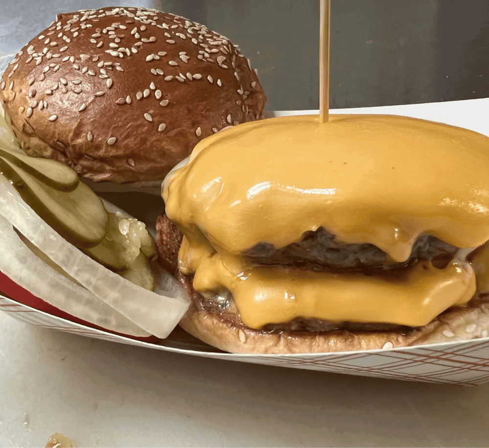 Cheeseburger with melted cheddar, pickles, and sesame seed bun, served with onion slices.