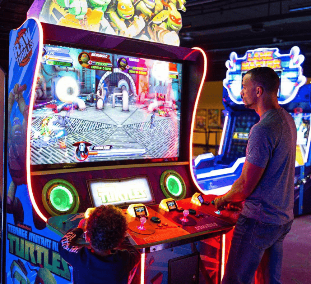 Arcade game console with Teenage Mutant Ninja Turtles theme, colorful lights, and players enjoying gaming fun.