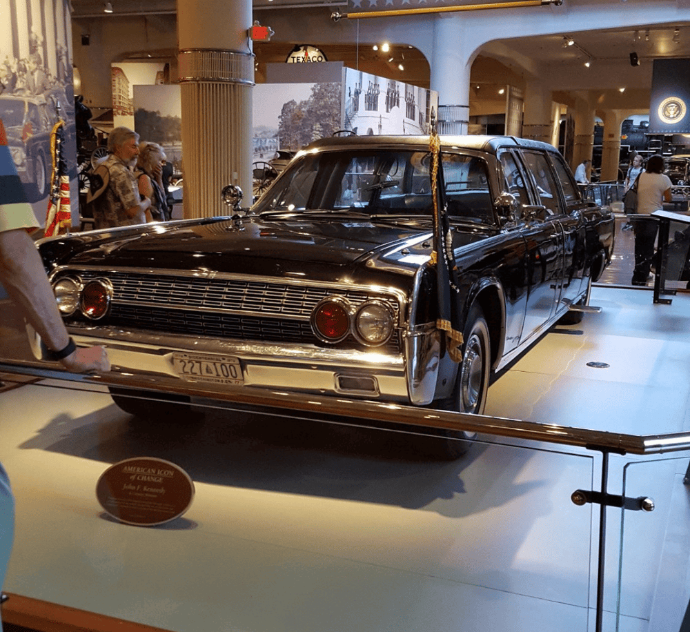 Black vintage presidential limousine on display at a museum, with informational plaque nearby.