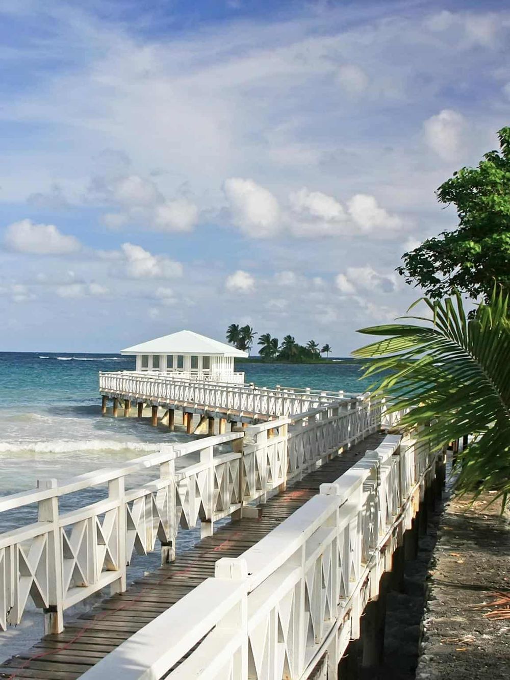 Scenic beachfront pier with a white gazebo, ocean view, tropical trees, perfect for relaxation and travel inspiration.