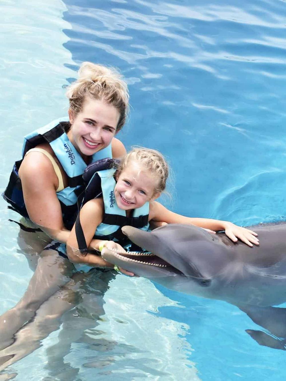 Girls and child enjoying dolphin encounter at water park, smiling and holding dolphin.