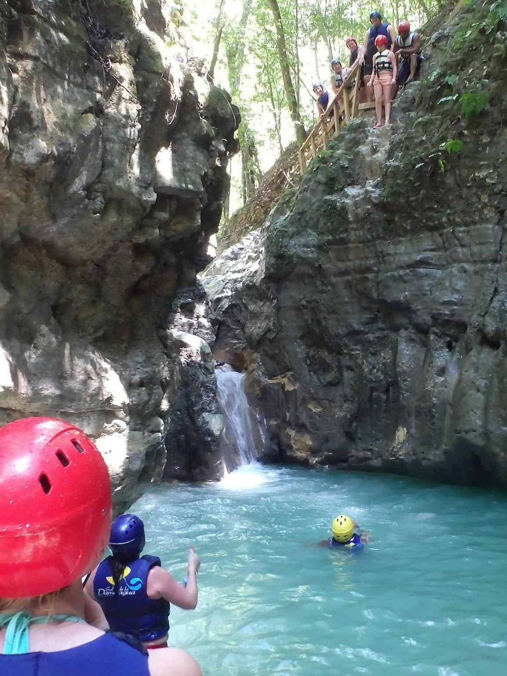 1. People hiking and swimming in a canyon stream with rock walls and lush greenery.