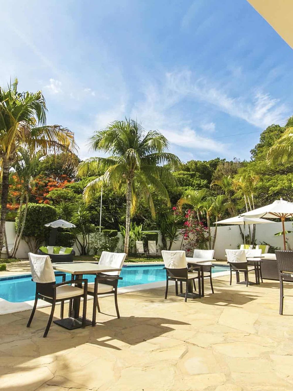 Tropical poolside oasis with lounge chairs, umbrellas, and lush greenery on a sunny day.