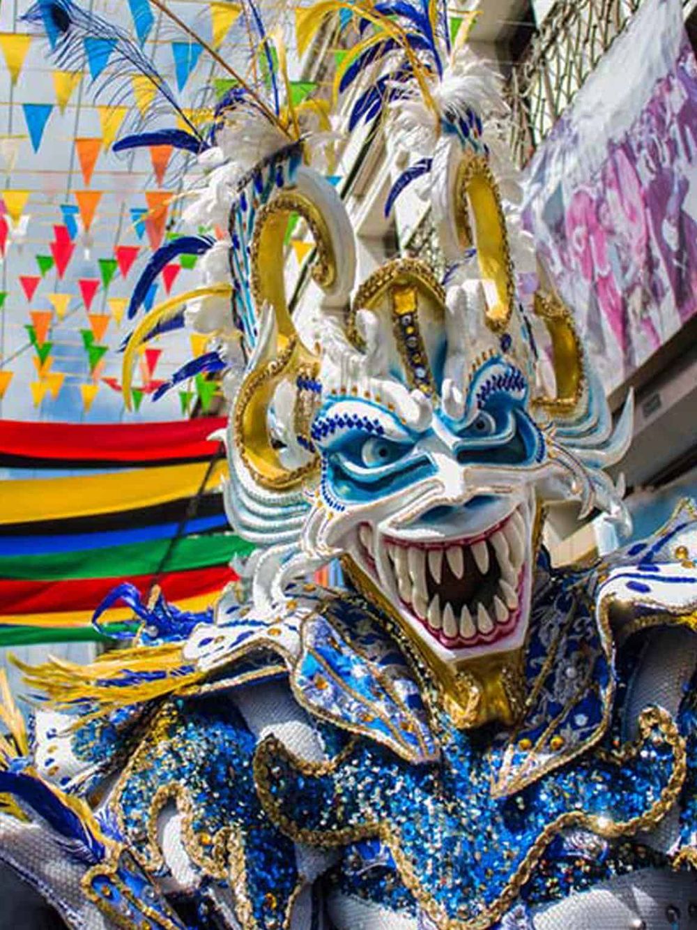 Vibrant carnival mask with intricate blue, gold, and white details, feathers, and embellishments.