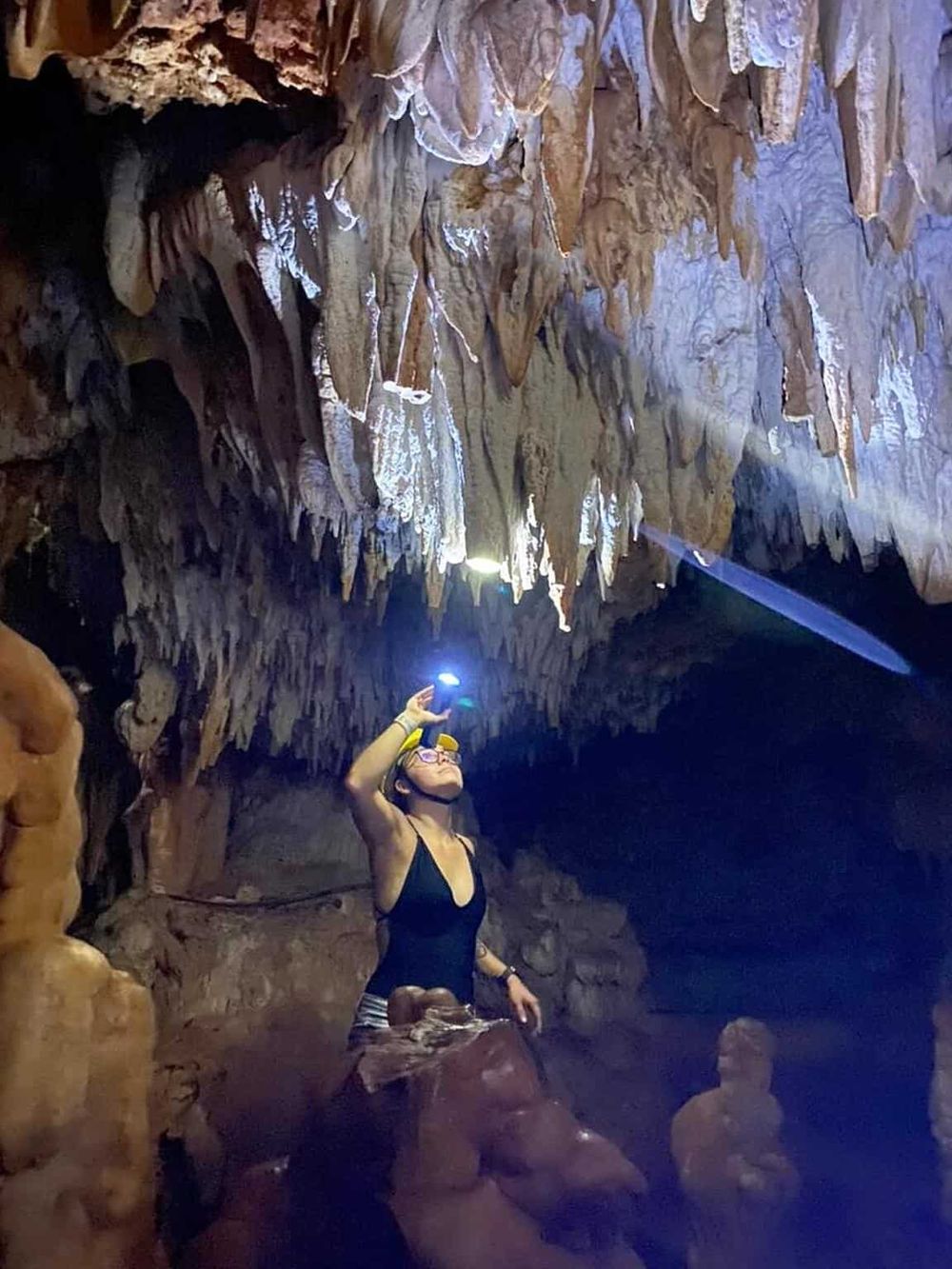 Intriguing cave exploration scene with a woman using a flashlight to discover stalactites and stalagmites inside a cavern.