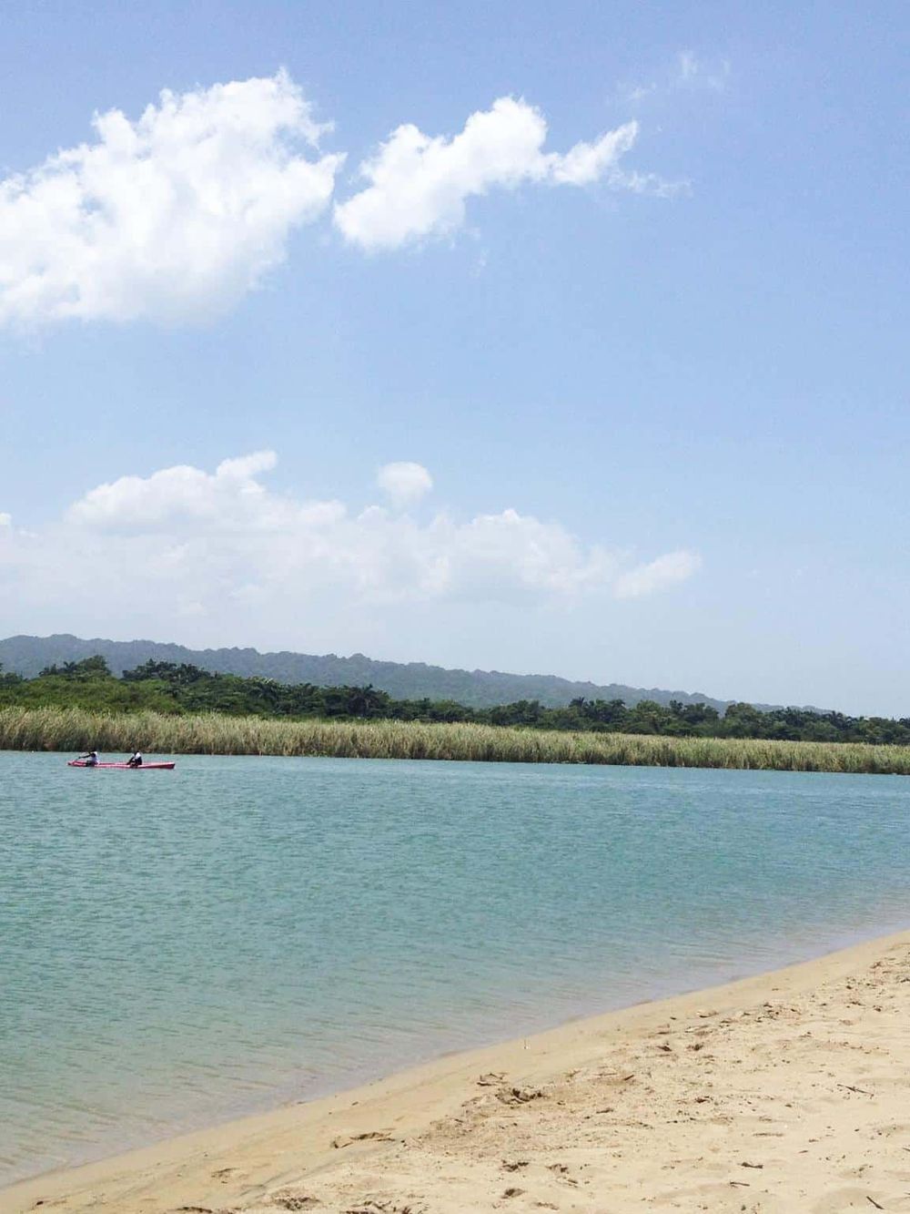 Serene lake scenery with kayakers, lush greenery, and mountains on the horizon for outdoor adventure seekers.