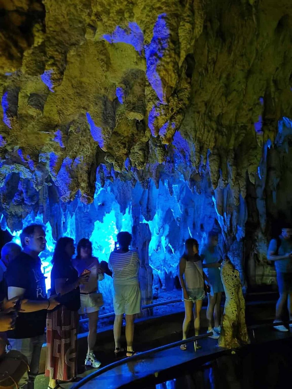 Stalactites in a vibrant, illuminated cave with visitors exploring underground formations.