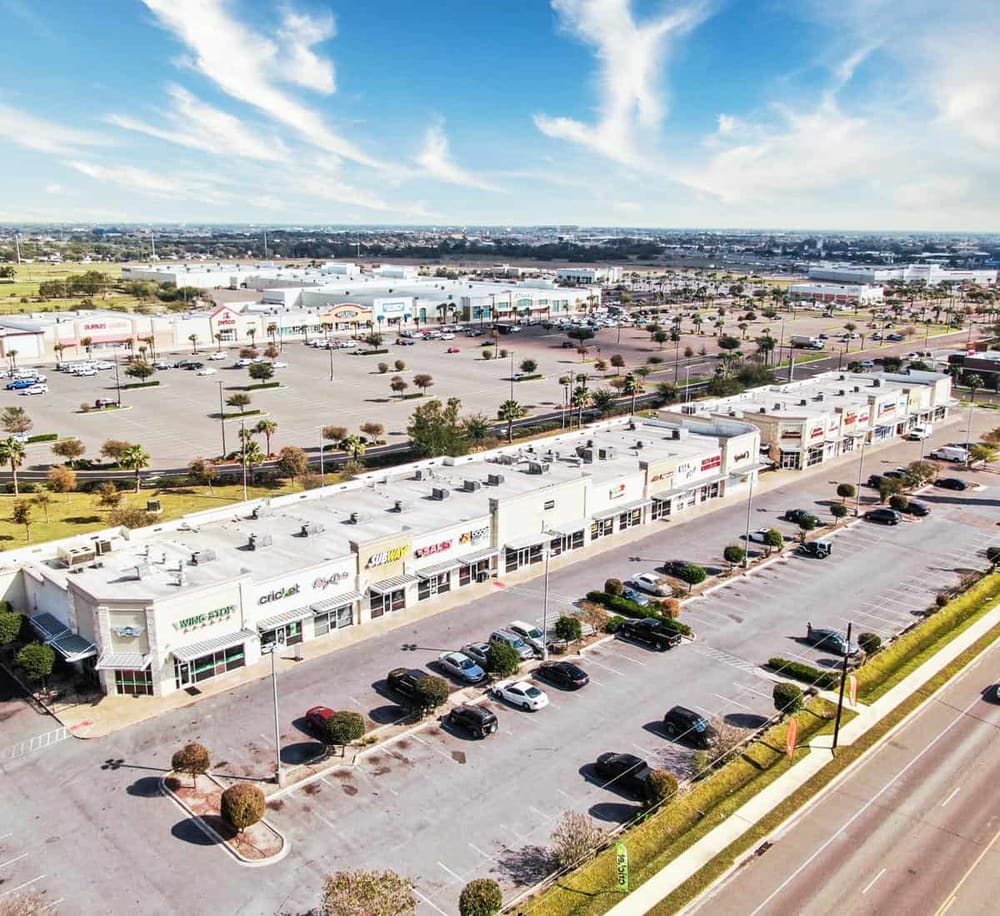 Bright shopping mall with retail stores, parking lot, and clear sky; ideal for retail and commercial property SEO.