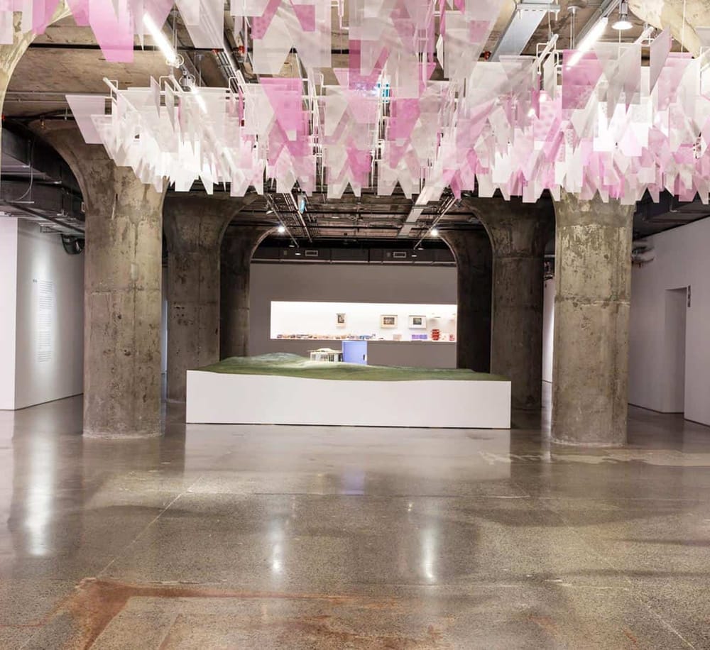 Colorful hanging art installation with concrete pillars in an art gallery space.