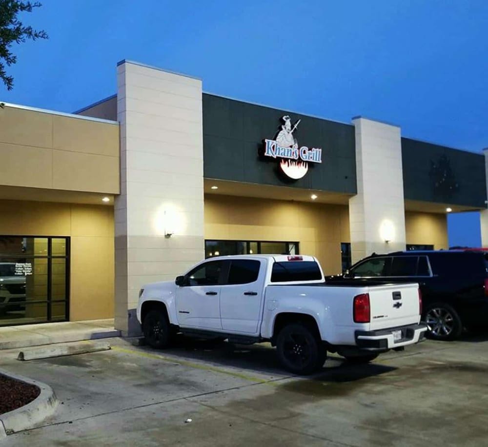 White pickup truck parked in front of Khan's Grill restaurant at dusk.