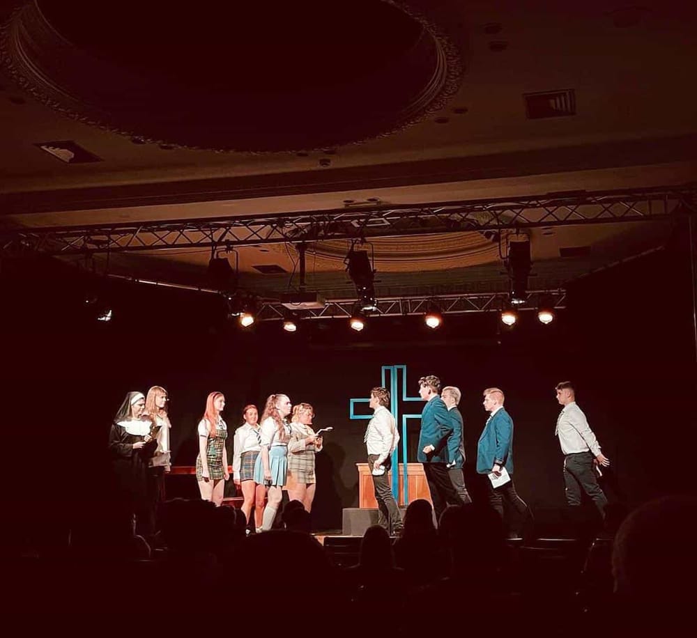 Bright stage scene with actors performing in a theatrical production, emphasizing drama and entertainment.