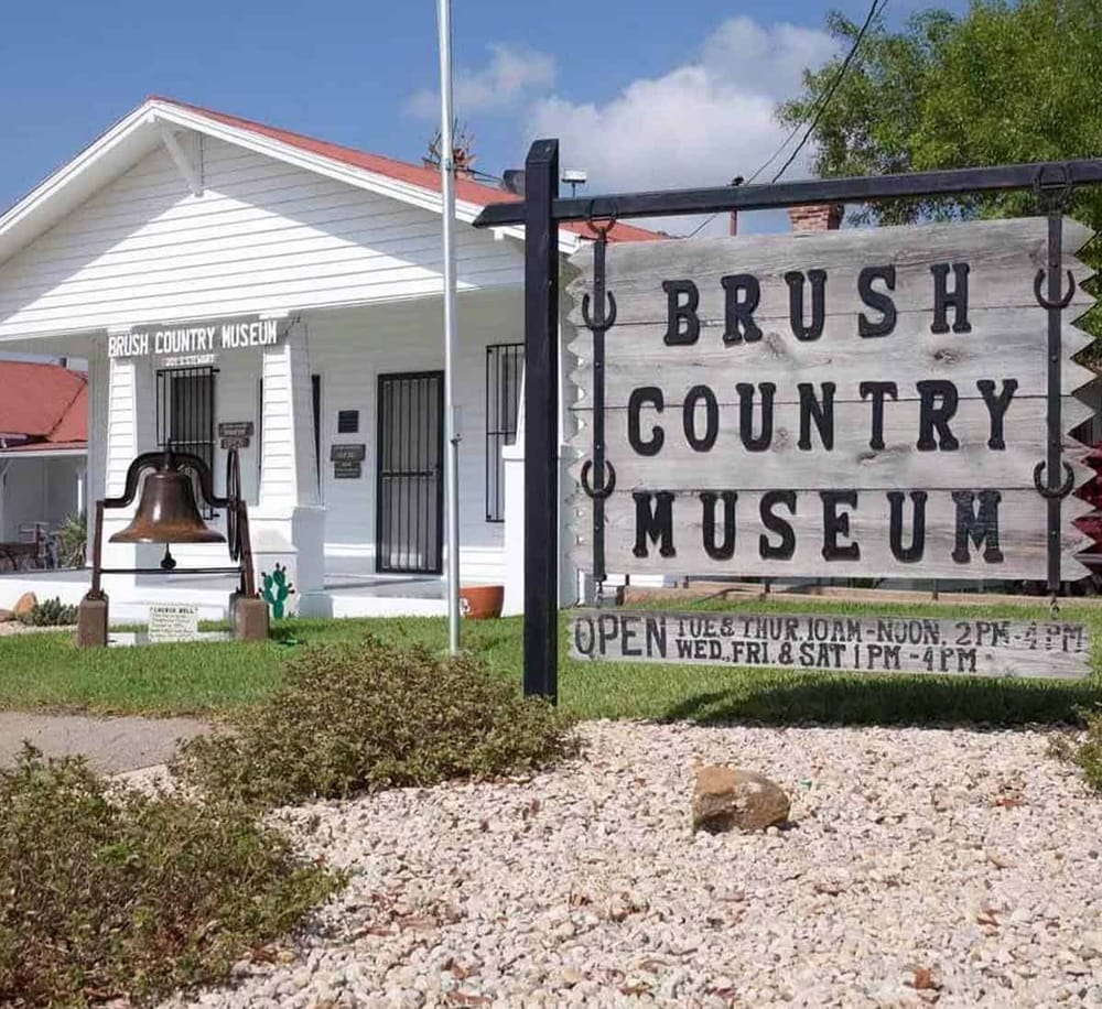 1. Vintage Brush Country Museum sign outside quaint white building with bell.