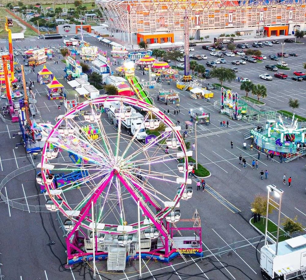 Colorful amusement park rides and games at night in a large parking lot.