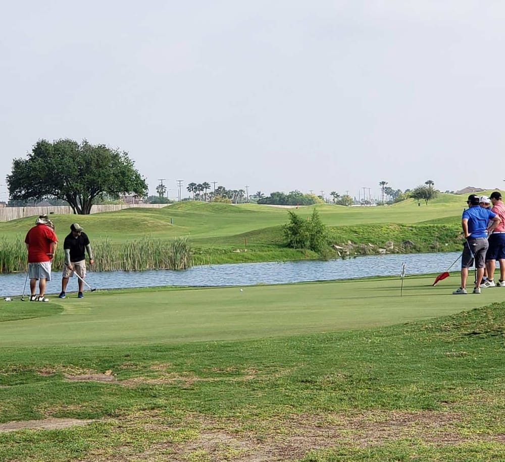 Golf course with players practicing putting by a pond, scenic views, and bright weather at QuestForDirections location.