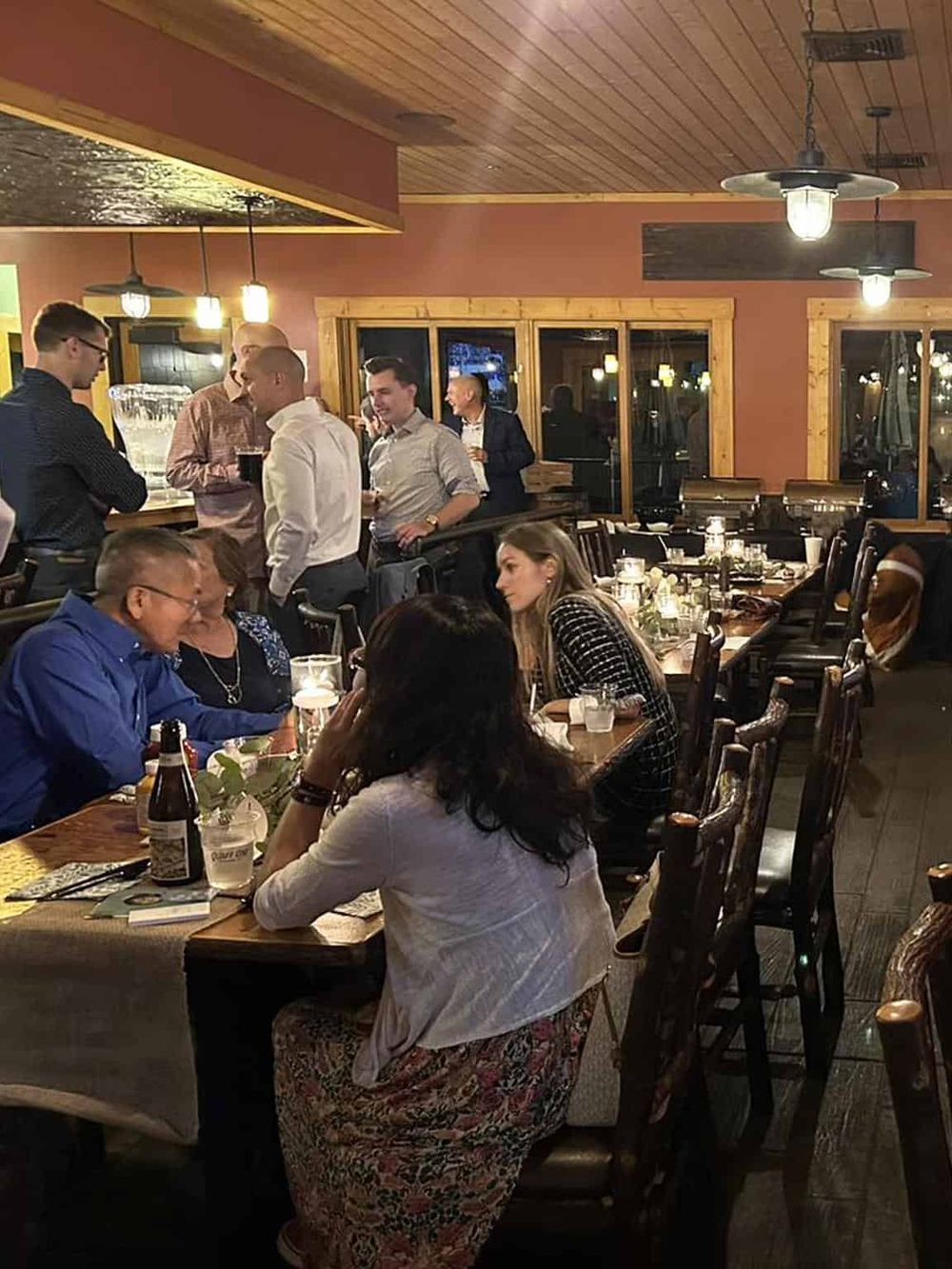 Cozy restaurant interior with people dining and socializing, warm lighting and wood accents.