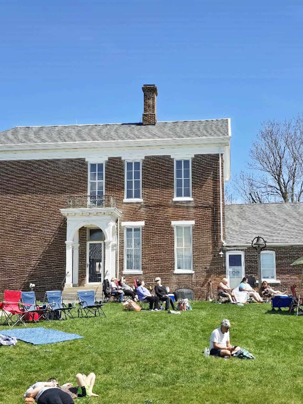 Restoring Social Trust: Seniors gather and relax outdoors on the lawn of a historic brick house during community event.
