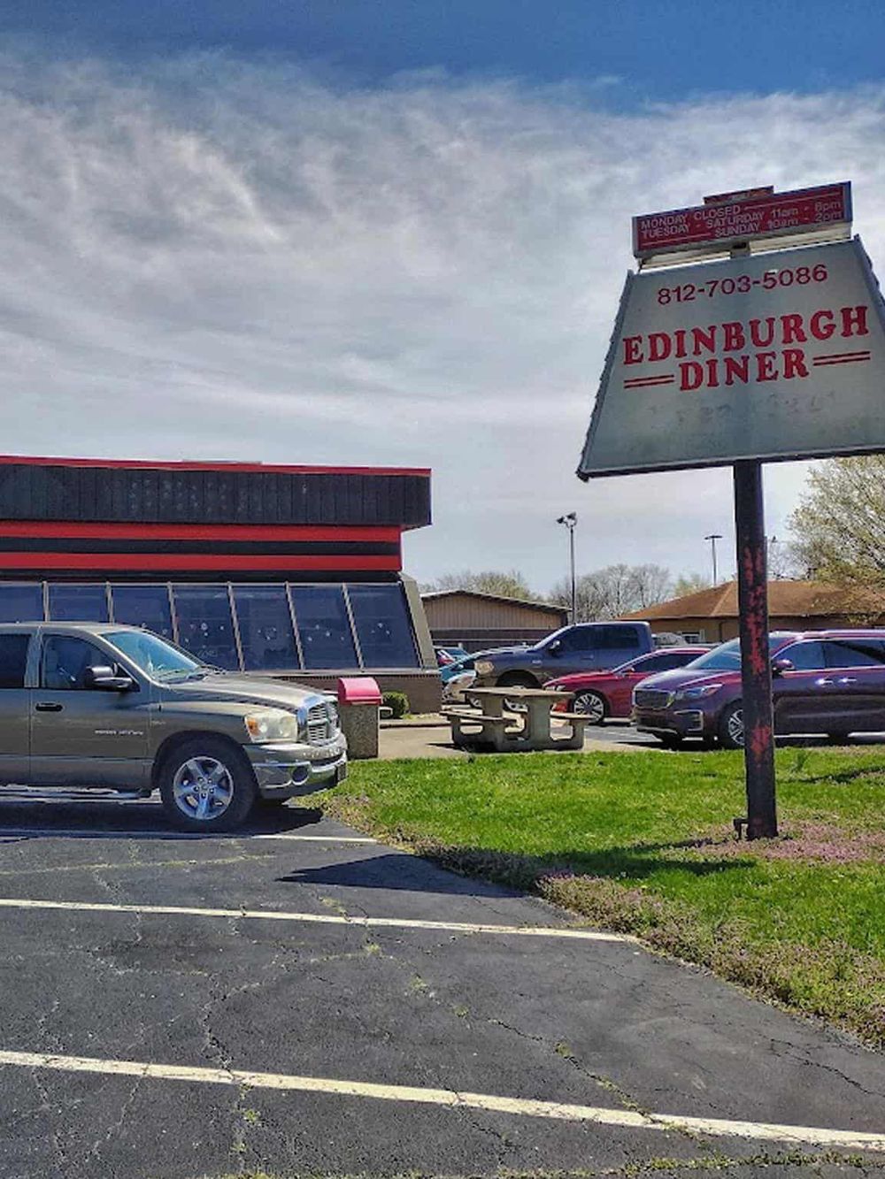 Vintage Edinburgh Diner sign in a parking lot with cars and a modern building in the background.