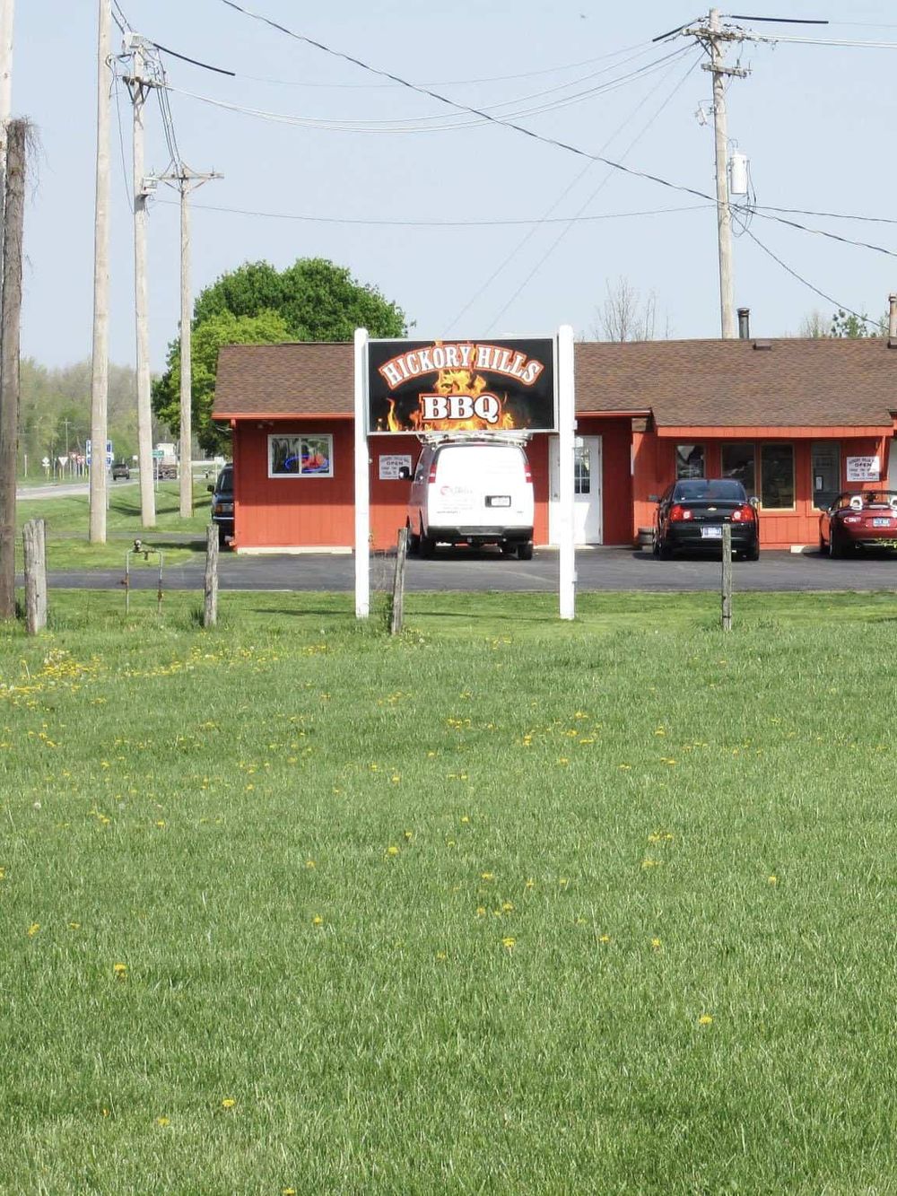 Vibrant red BBQ restaurant with outdoor parking and "Hickory Hills BBQ" sign, in a green grassy area.