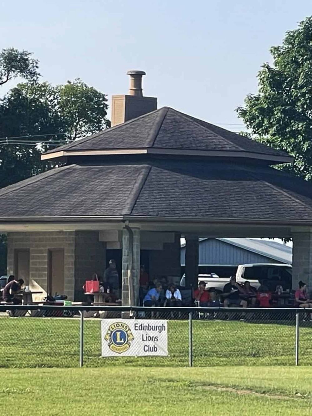 Quiet outdoor gathering at Edinburgh Lions Club pavilion with people seated and socializing.