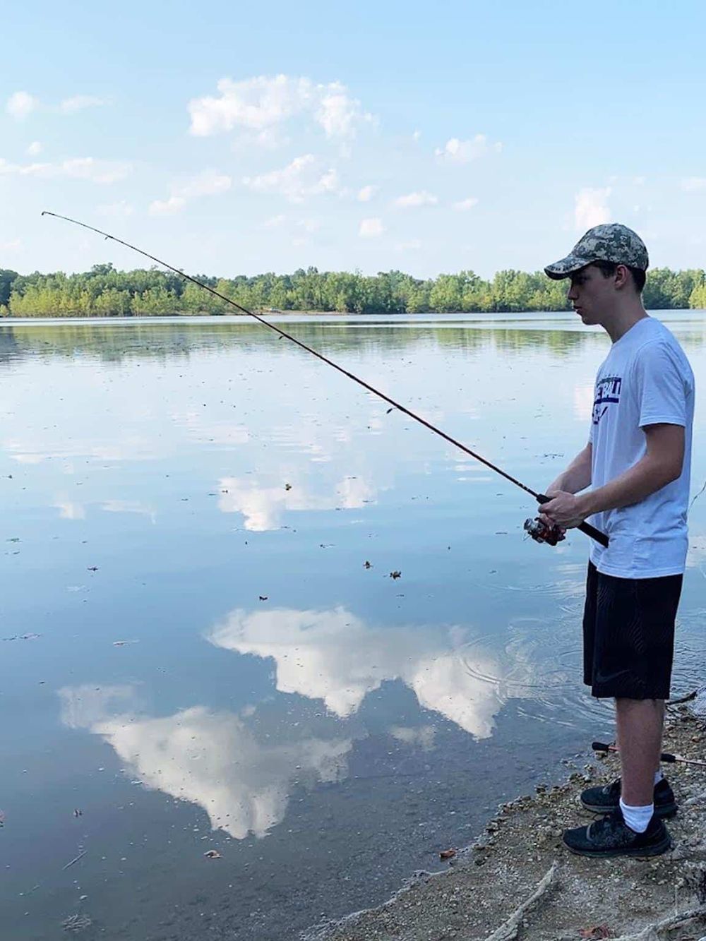 Fishing on a tranquil lake with lush greenery and blue skies, perfect for outdoor recreation and nature exploration.