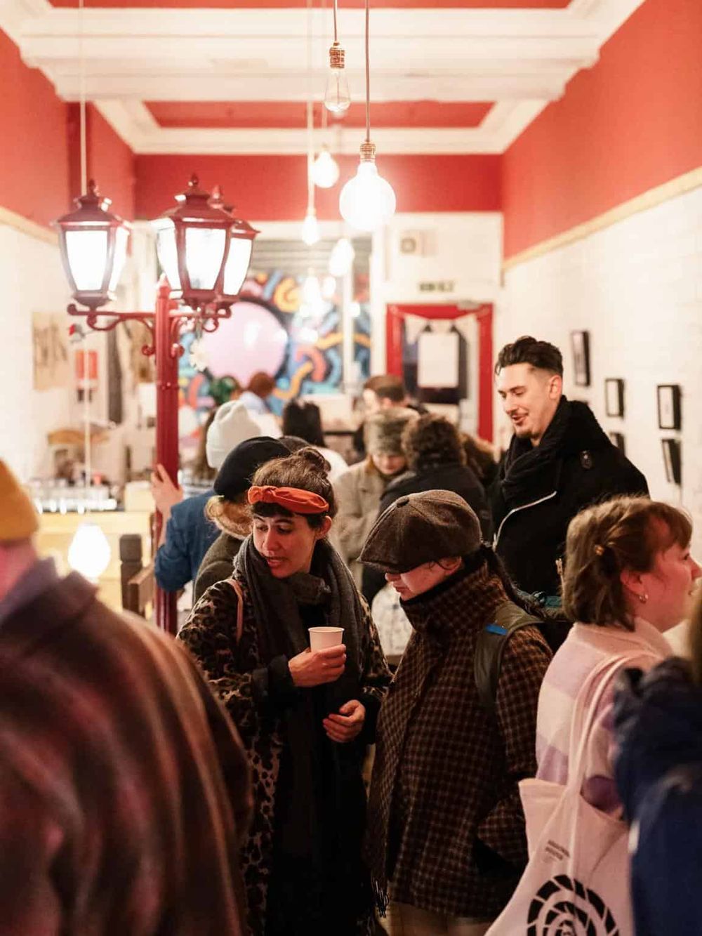 Bustling indoor scene with people enjoying coffee, vibrant red walls, and cozy lighting at QuestForDirections location.