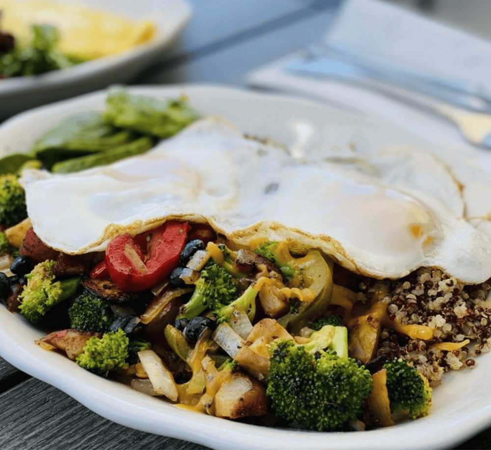 Fresh veggie breakfast bowl with a sunny side-up egg on top, served outdoors on a rustic table.
