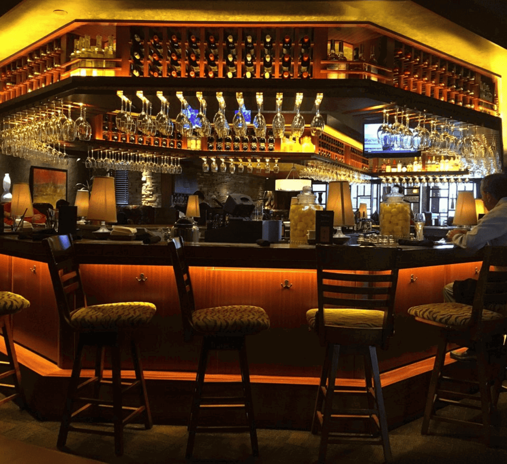 Elegant hotel bar with wine bottles and glassware display, cozy lighting, and inviting ambiance.
