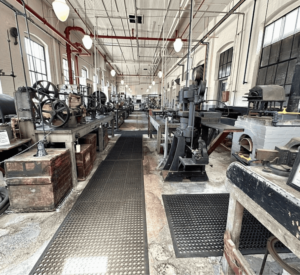 Vintage industrial workshop with metalworking machines and tools, well-lit with large windows.