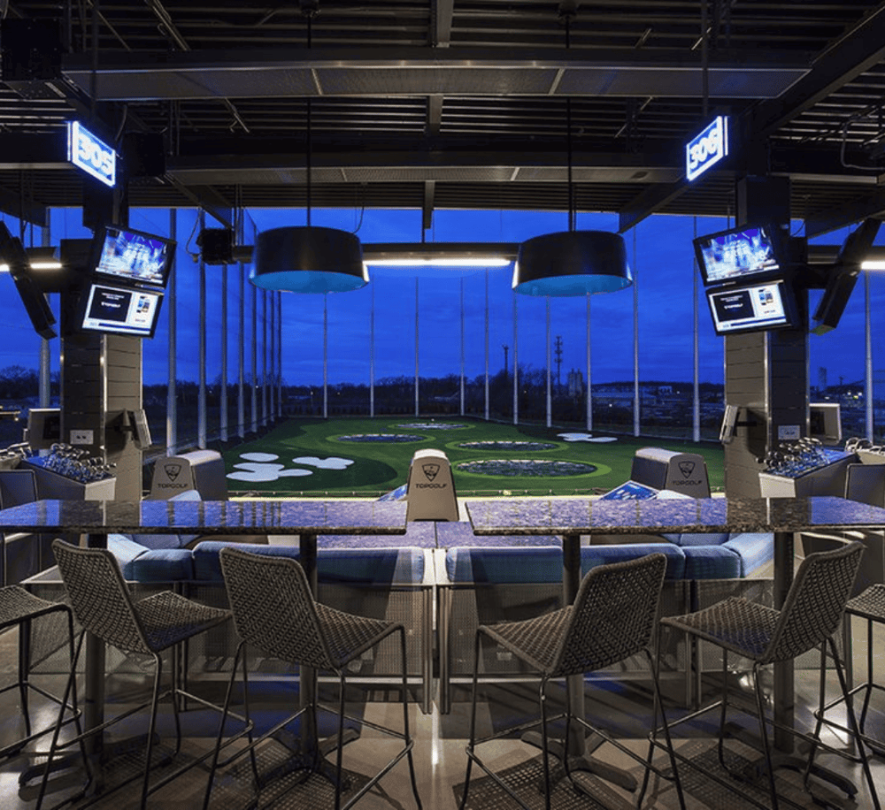 Aerial golf lounge with city view, modern interior, high-tech golf simulators.